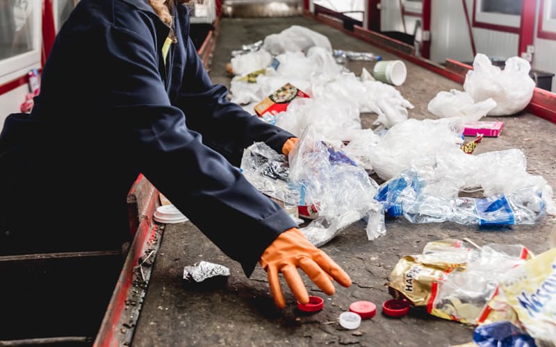 a person with orange gloves sorts plastic at a recycling plant
